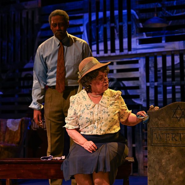 Older women in a hat on stage looking at a trunk.