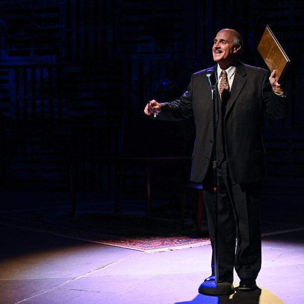 Older African American man singing in a suit on stage.