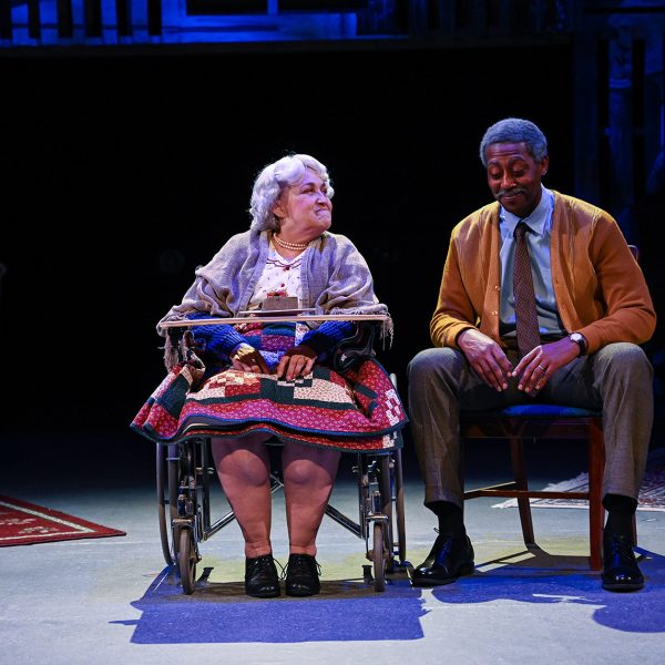 Older woman in wheelchair talking to man on stage.