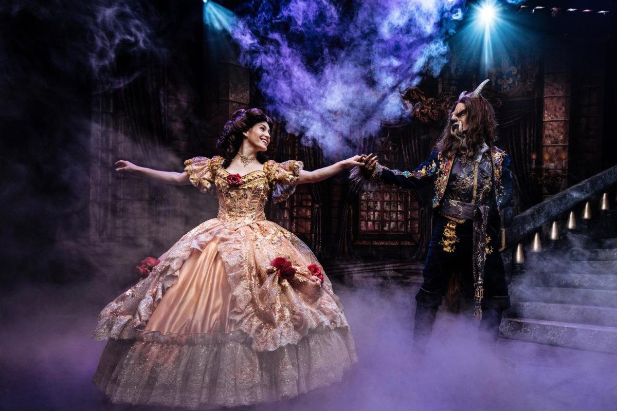 The character Belle in a ball gown dancing with the Beast in full mask and a suit.