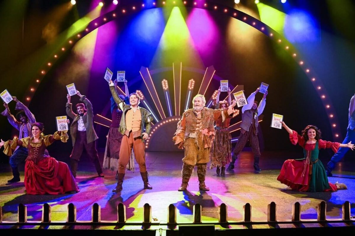 Group on stage wearing medieval clothing holding playbills in the air.