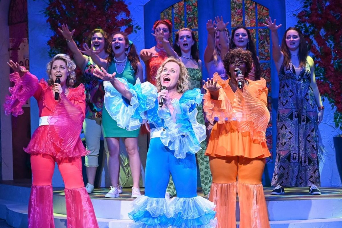 Women singing on stage in brightly colored bell bottoms.