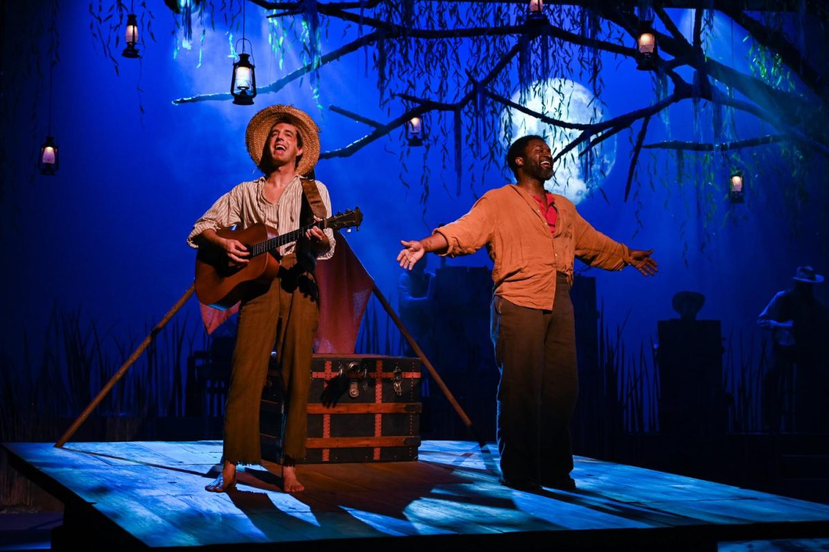 2 men singing on stage barefoot. One is playing a guitar.