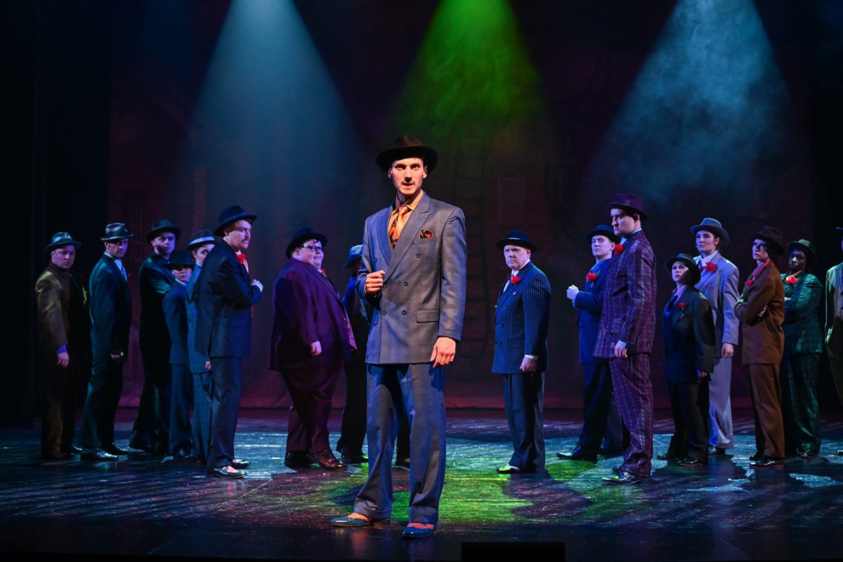 Ensemble cast wearing suits and hats on stage.