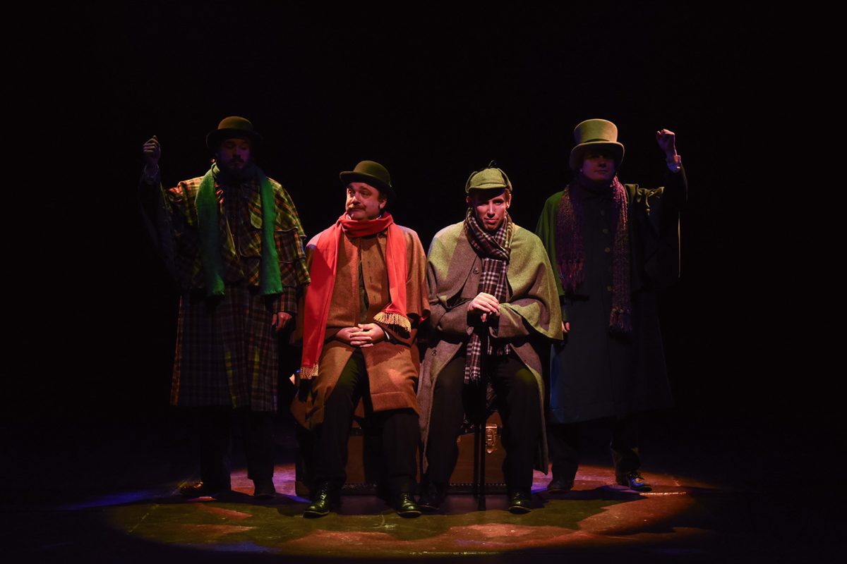 4 men on stage wearing hats and trench coats.