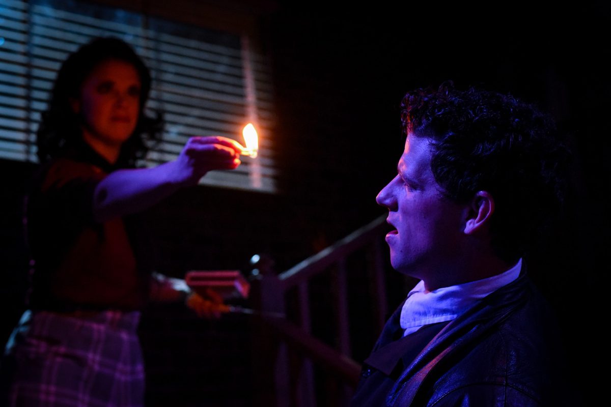 Woman holding a match in front of a man's face.