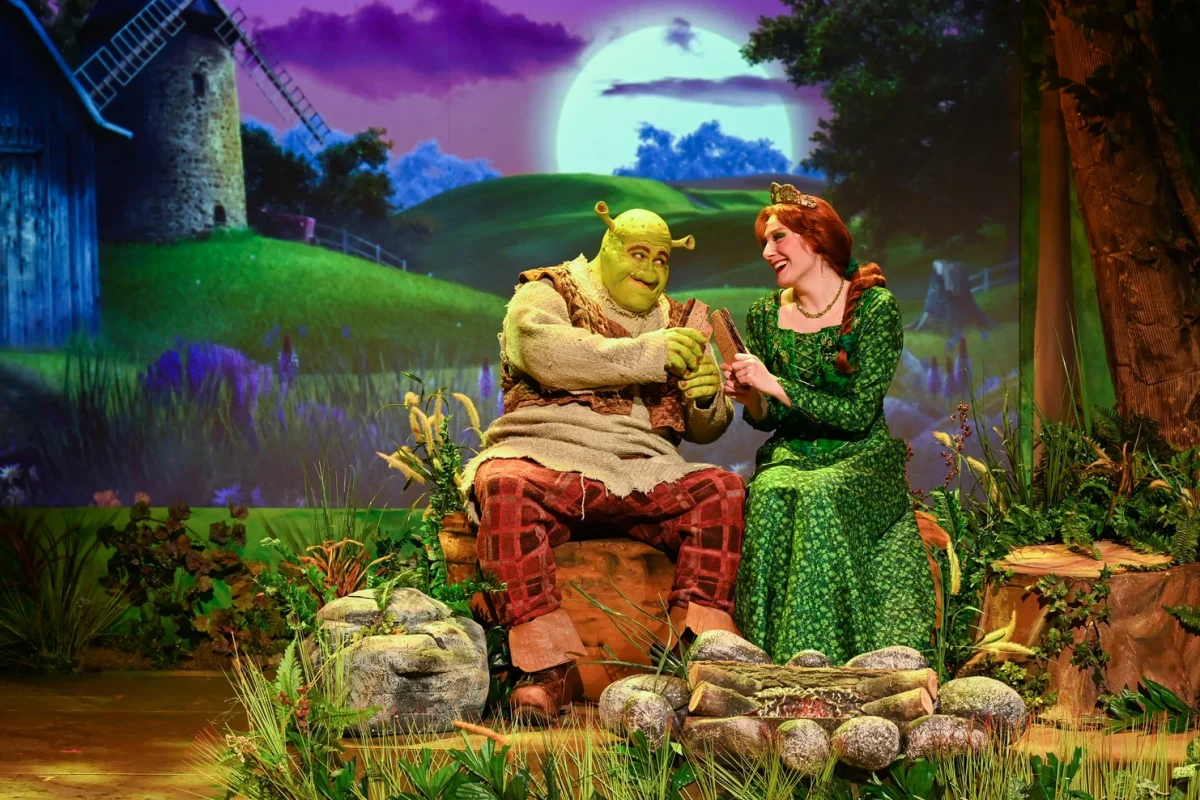 Shrek and Fiona on stage with a sunset backdrop.